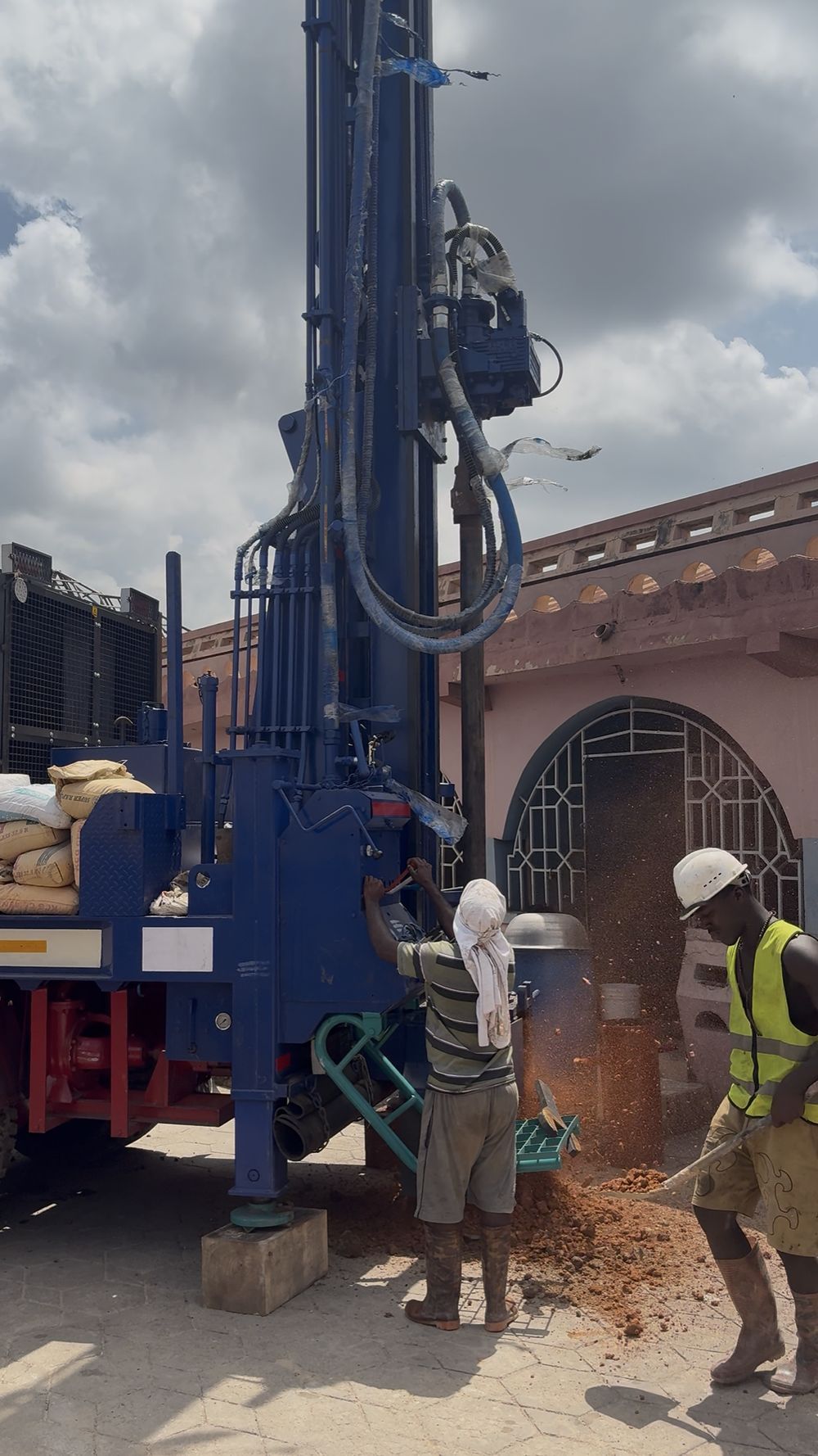 An Apex crew drilling a borehole beside a house, cuttings piled at the collar